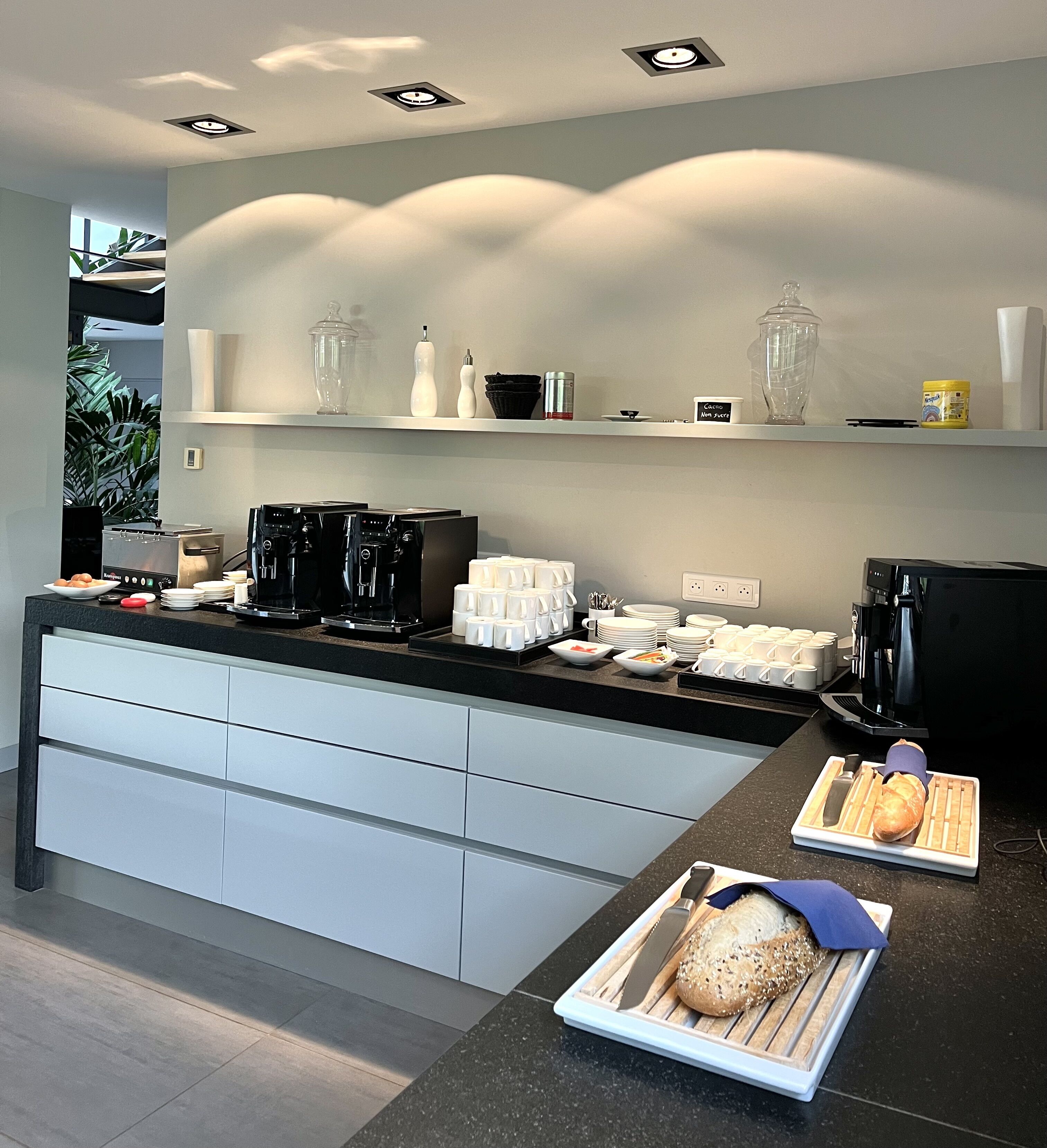 A modern kitchen with a central island, coffee machines, and a bread display.