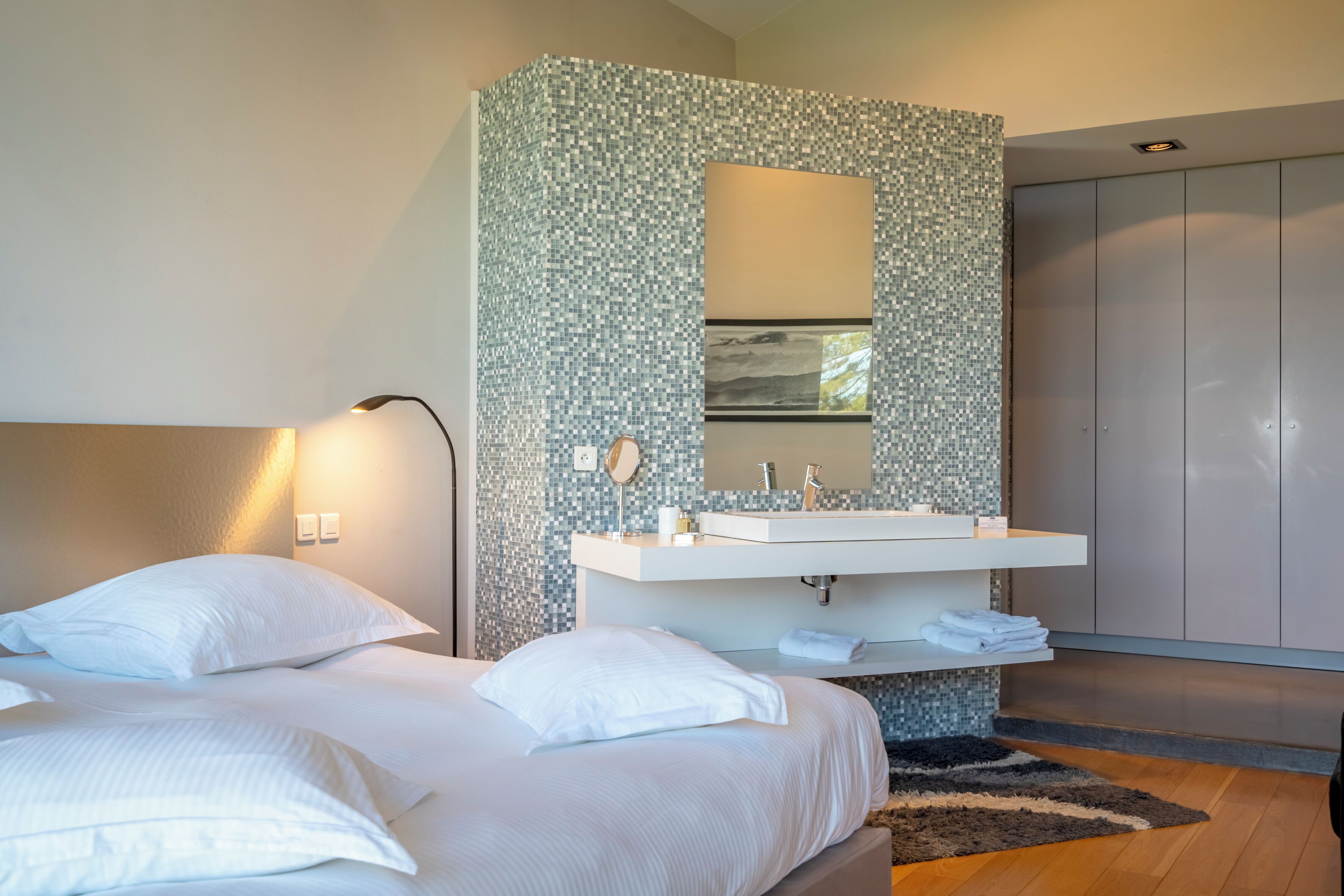 Una habitación de hotel moderna con una cama grande, un tocador blanco con espejo y un armario.