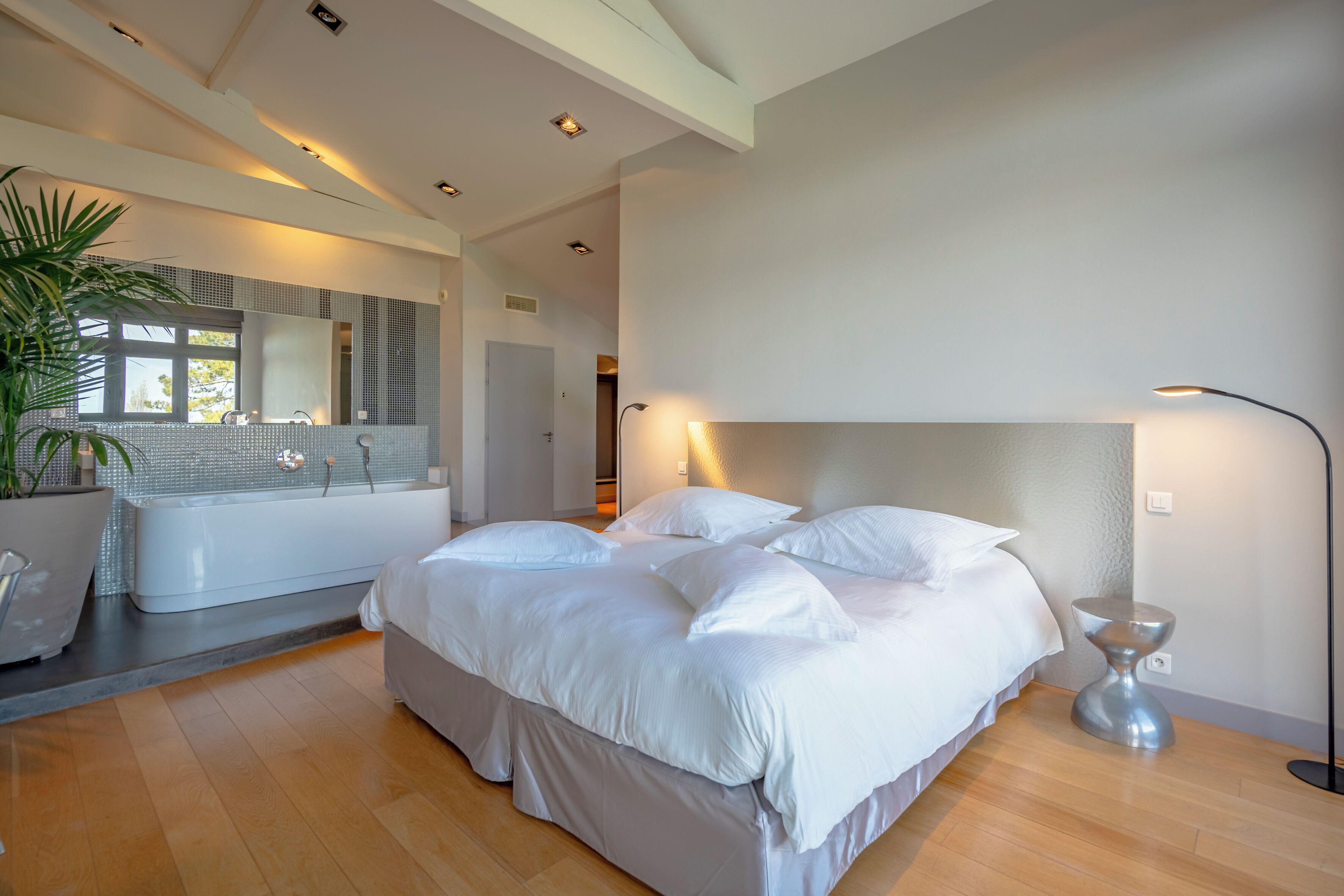 A modern bedroom with a large bed, a built-in bathtub, and a potted plant.