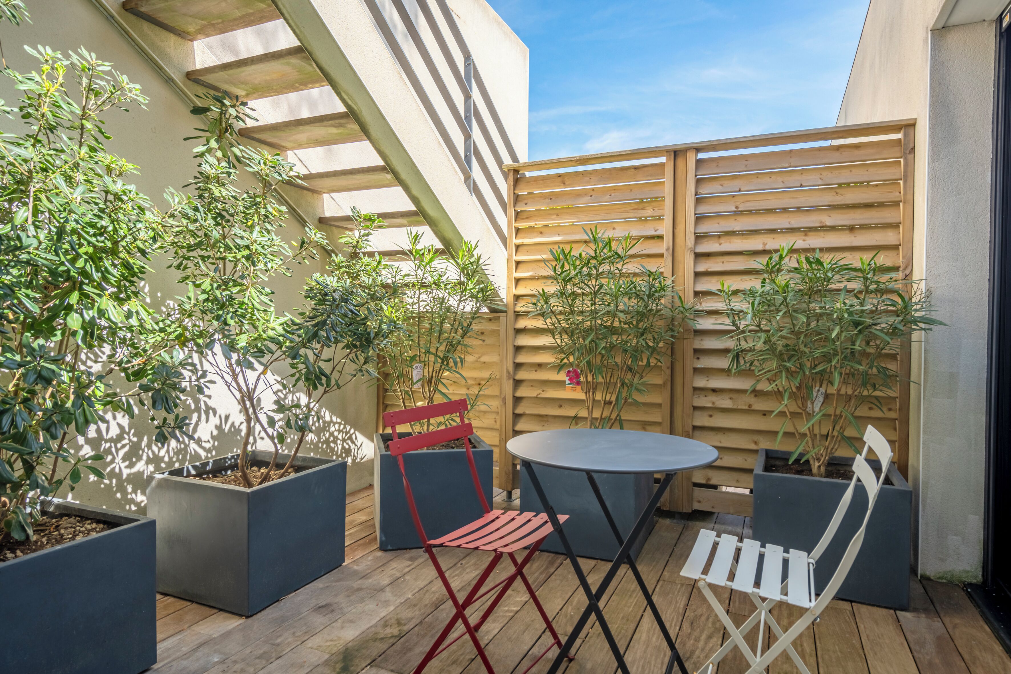 A patio with a round table and two chairs, surrounded by potted plants and a wooden fence.