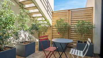 A patio with a round table and two chairs, surrounded by potted plants and a wooden fence.