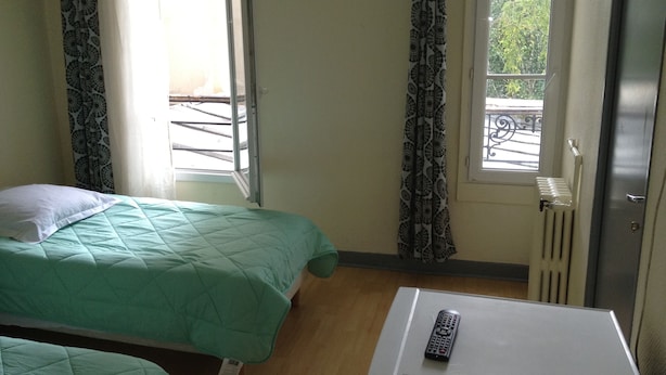 A room with two beds, a white table, a window with a view, and a radiator. - Au Royal Mad Hotel (Paris)
