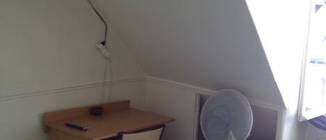 A room with a desk, chair, and a standing fan.