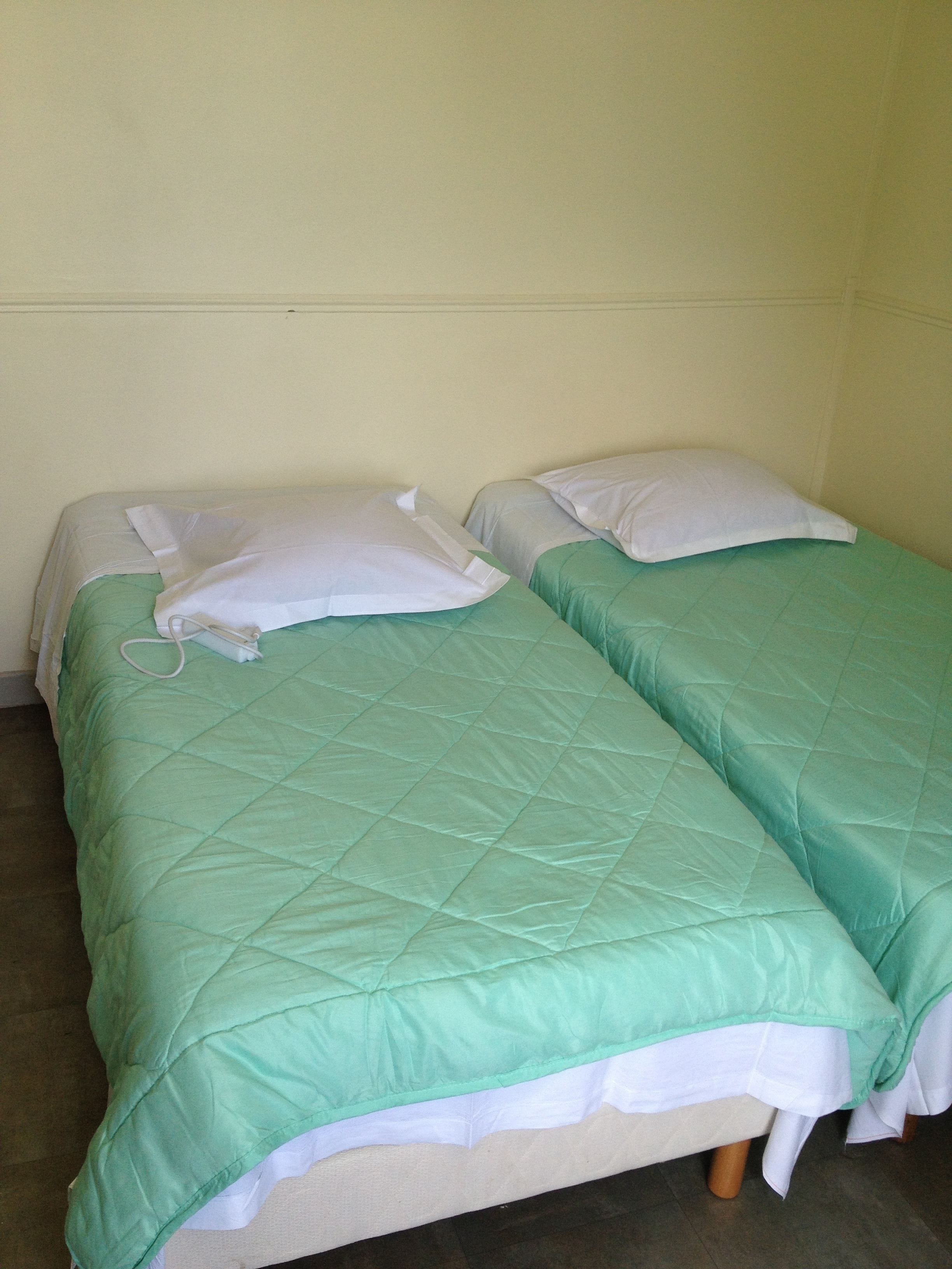 A twin bed with a green quilt and white pillows in a room with plain walls.