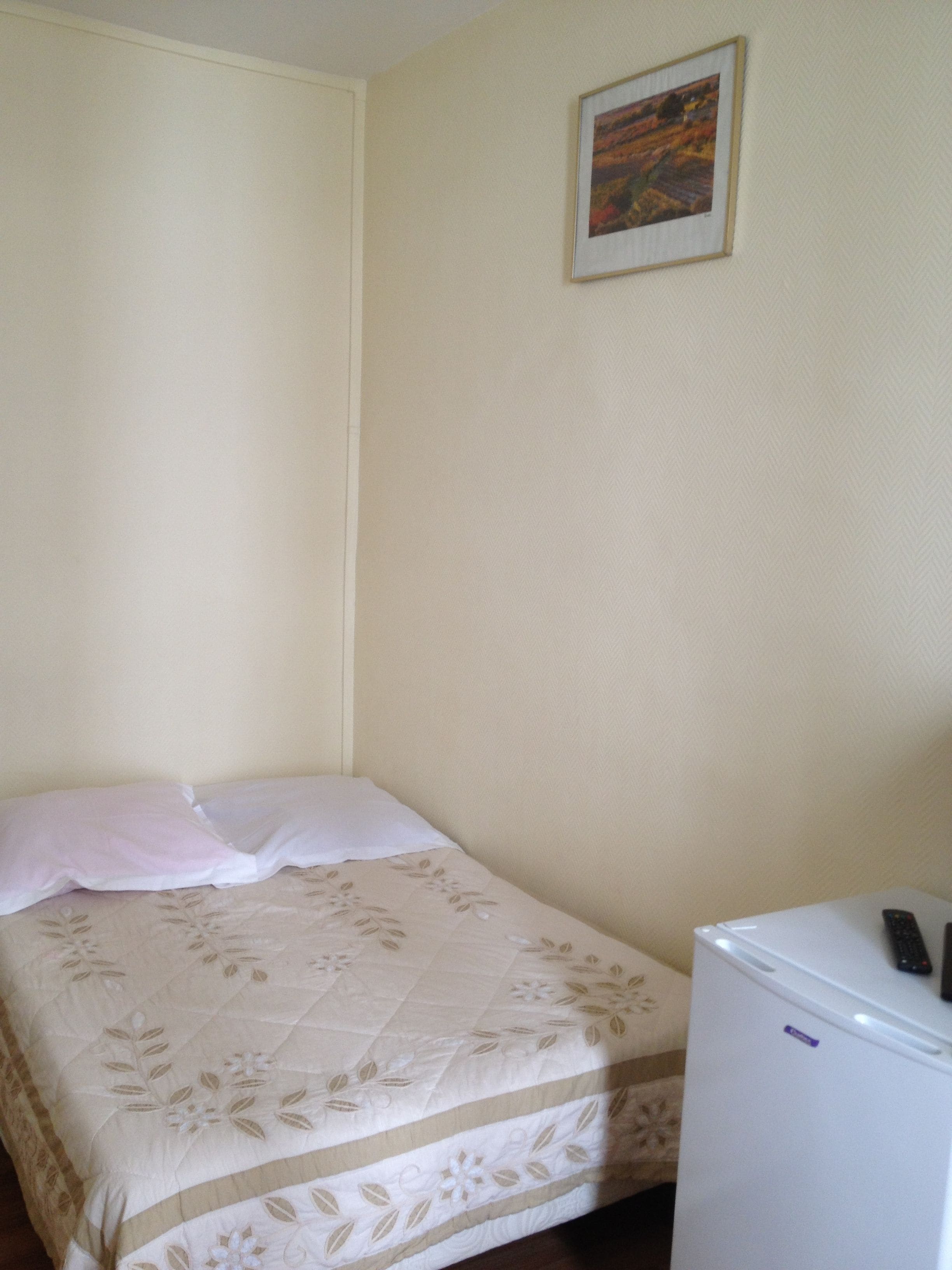 A small, single-bed room with a plain wall and a framed picture.