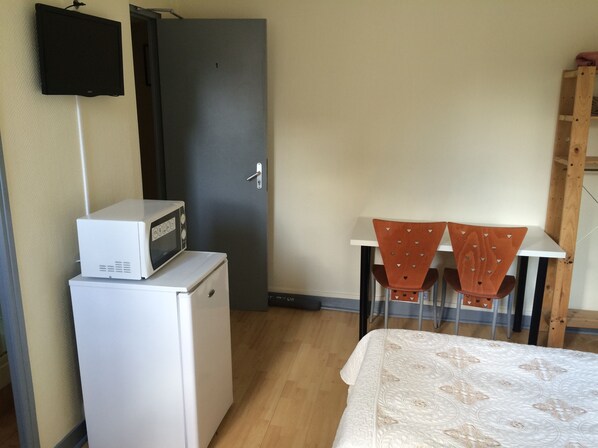 A compact room with a bed, a small refrigerator, a microwave, a TV mounted on the wall, and two chairs with a table. - Au Royal Mad Hotel (Paris)