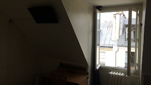 A room with a sloped ceiling, a radiator, and a window with a view of buildings outside. - Au Royal Mad Hotel (Paris)