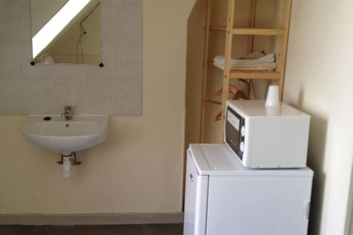 Un baño con lavamanos blanco, un espejo y una repisa de madera con toallas dobladas.