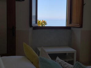 A bedroom with a bed, a bedside table, and a window overlooking the sea.