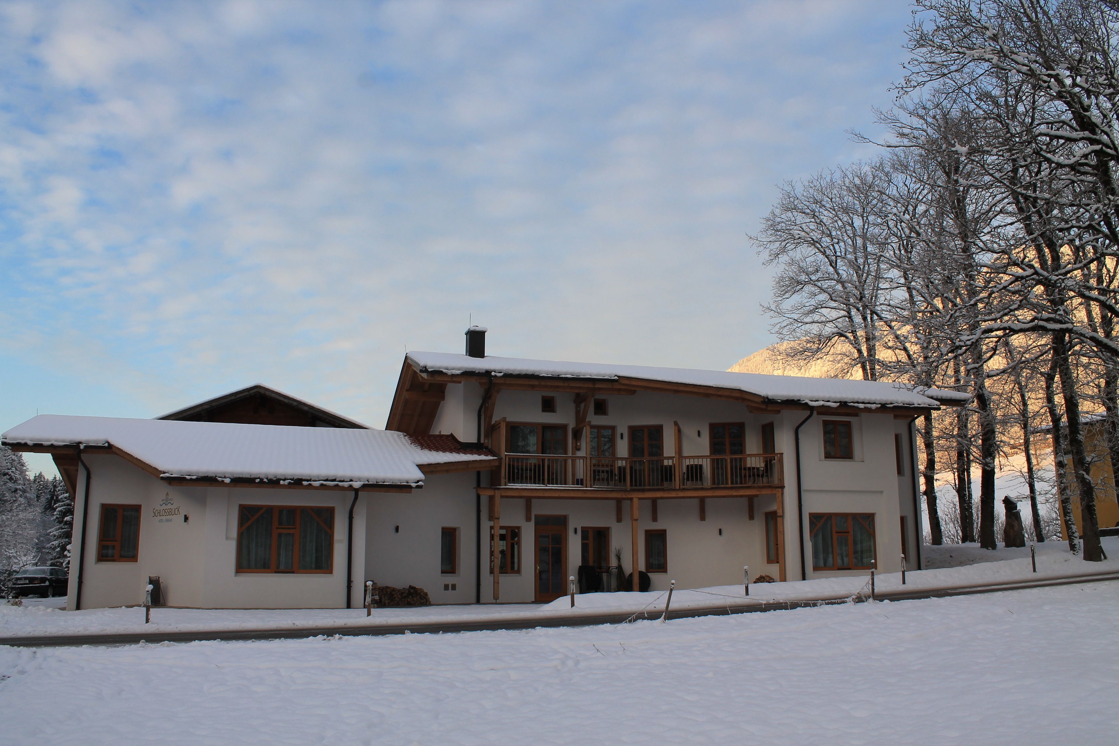 Un chalet à deux étages doté d’un balcon, entouré d’arbres couverts de neige et avec une montagne en toile de fond.
