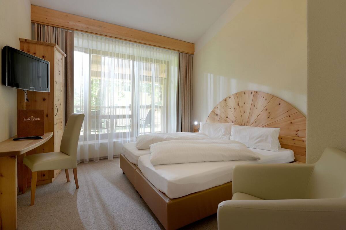 A hotel room with a bed, a desk, a TV, and a chair.