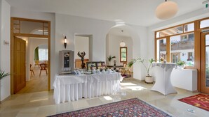 A hotel lobby with a coffee station, a reception desk, and a view of the outside. - Hotel Schlossblick (Angerberg)