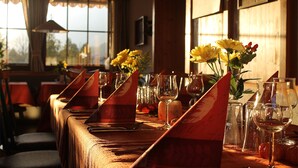 A restaurant with a long table set for a meal, glasses of wine, and a vase of yellow flowers. - Hotel Schlossblick (Angerberg)