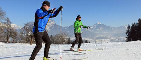 Two people cross-country skiing on a snowy landscape with mountains in the background.