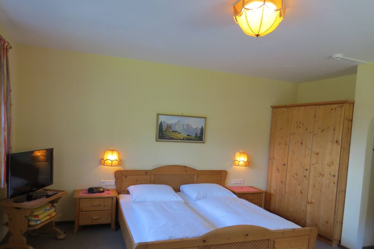 A bedroom with a wooden bed, two bedside lamps, a television, and a wardrobe.