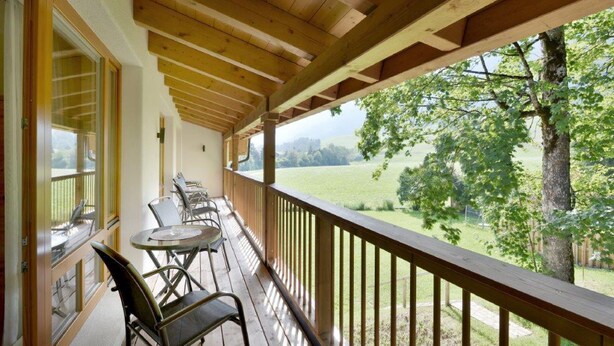 A covered outdoor area with a wooden ceiling, a table with chairs, and a view of a green landscape. - Hotel Schlossblick (Angerberg)