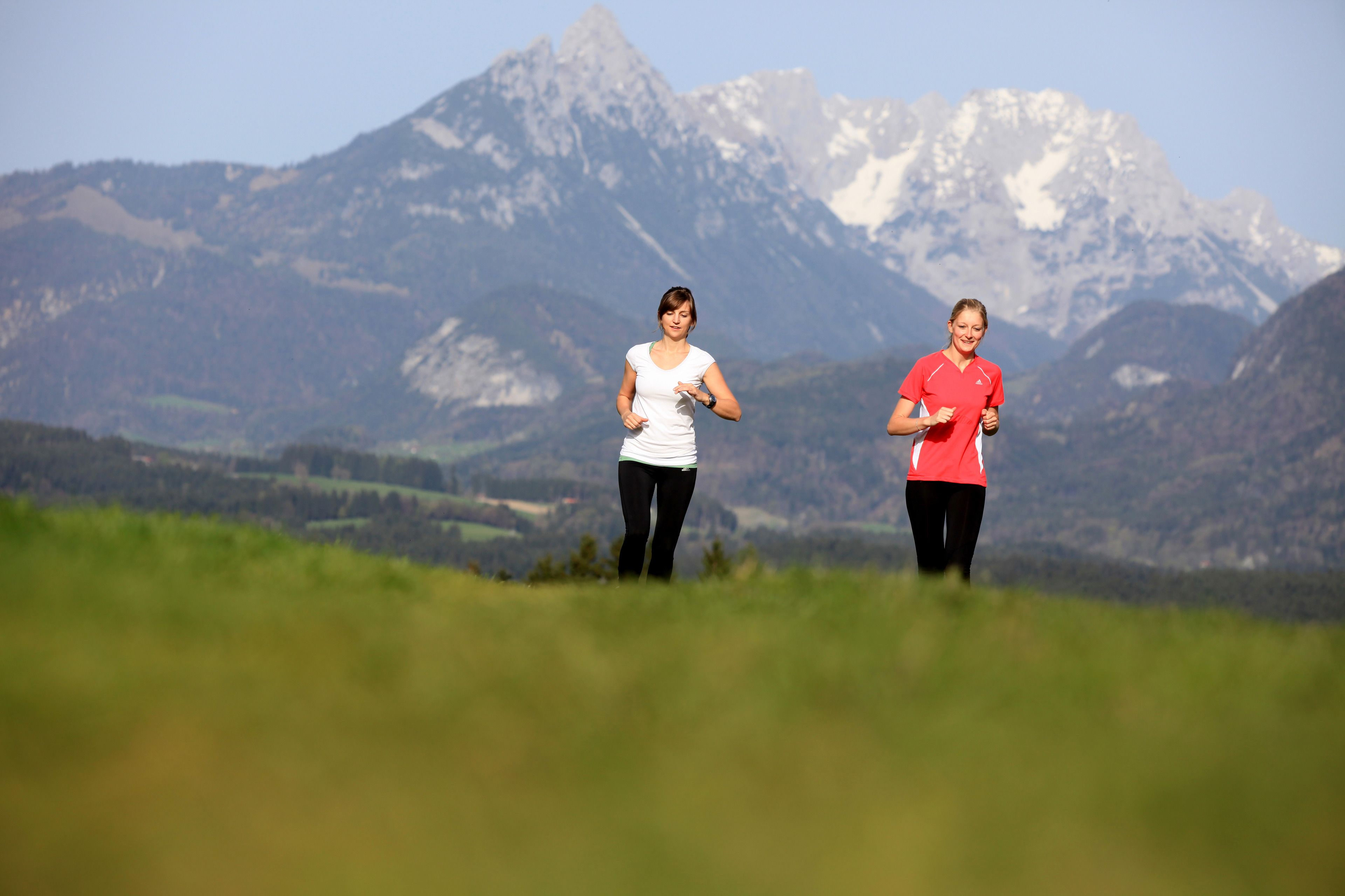 Two people jogging on a grassy field with a mountainous backdrop.