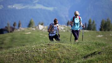 Two people hiking on a grassy hill with mountains in the background.