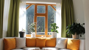 A living room with a sofa, green curtains, and potted plants. - Hotel Schlossblick (Angerberg)