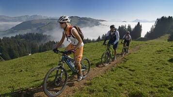 Tres ciclistas en un sendero de montaña, con vistas a montañas y nubes distantes.