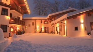 A snow-covered courtyard with a building featuring a balcony and a Christmas tree. - Hotel Schlossblick (Angerberg)