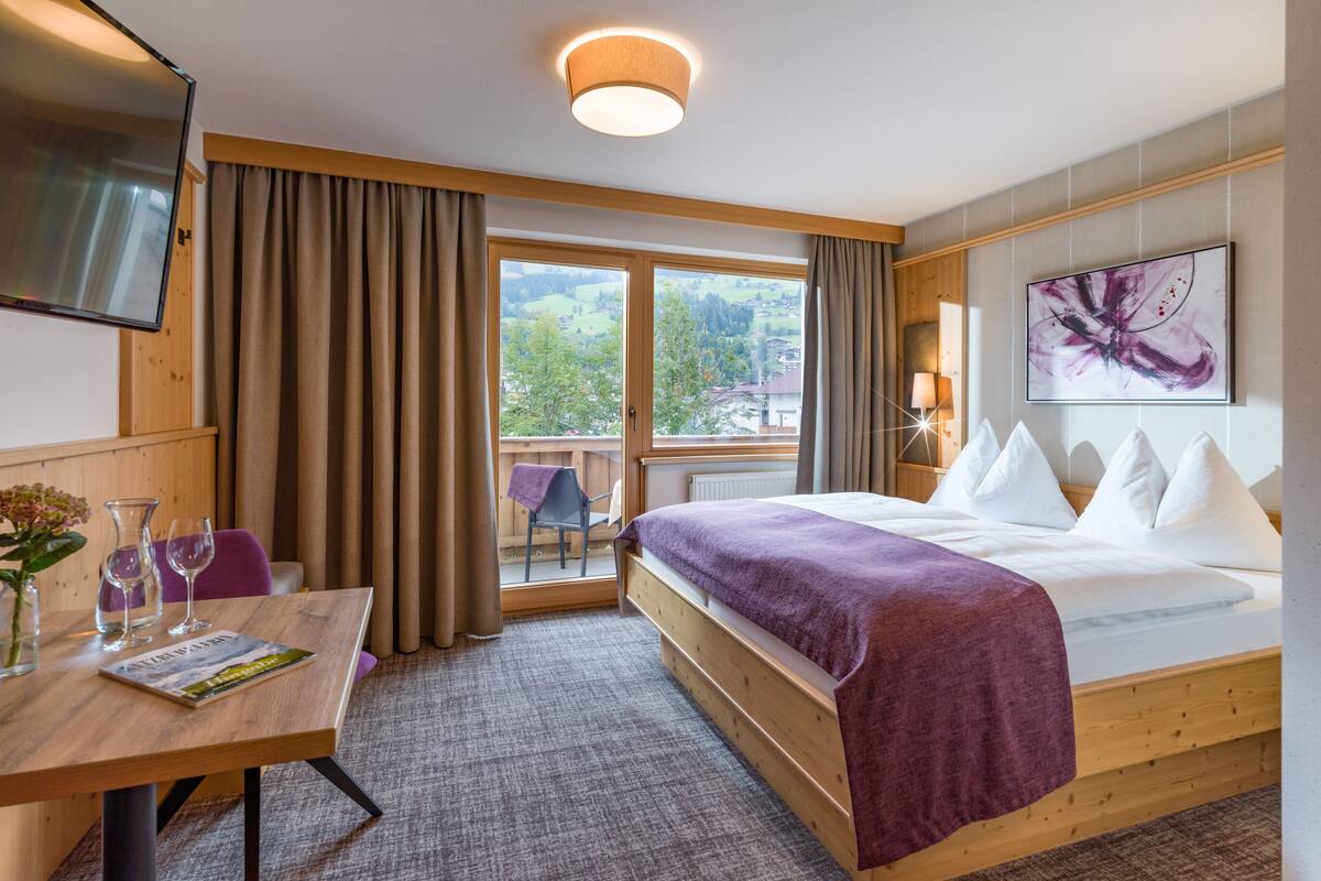 Ein Hotelzimmer mit Bett, Schreibtisch mit Stuhl, Fernseher, einem Fenster mit Vorhängen und einem Bild an der Wand.