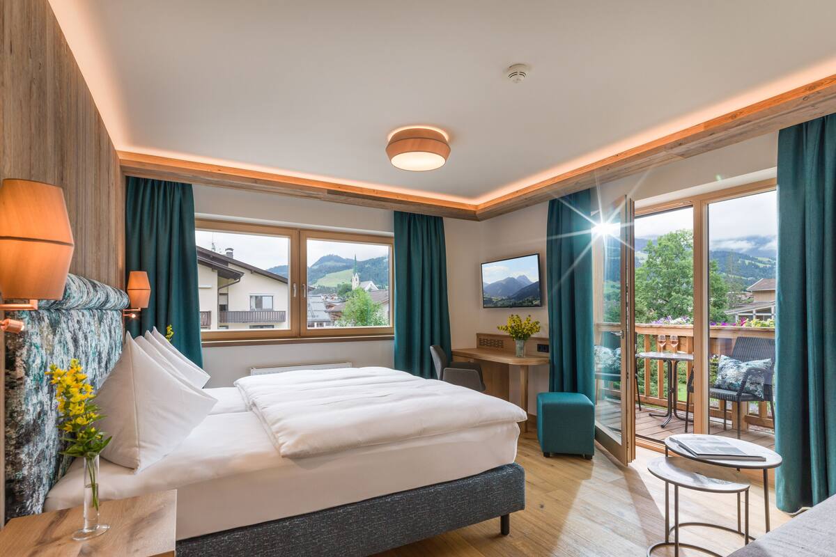 Ein Hotelzimmer mit einem großen Bett, einem Schreibtisch, einem Fernseher und einem Balkon mit Bergblick.