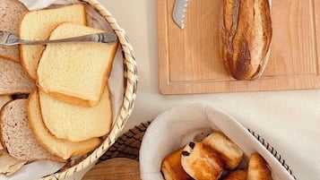 Ett bord med bröd, en kniv, en korg med croissanter och en växt.