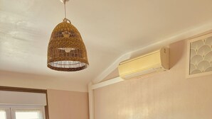 A bedroom with two beds, a hanging light fixture, a bedside table with a plant, and a wall-mounted air conditioner. - Hôtel le Nid (Argeles-sur-Mer)