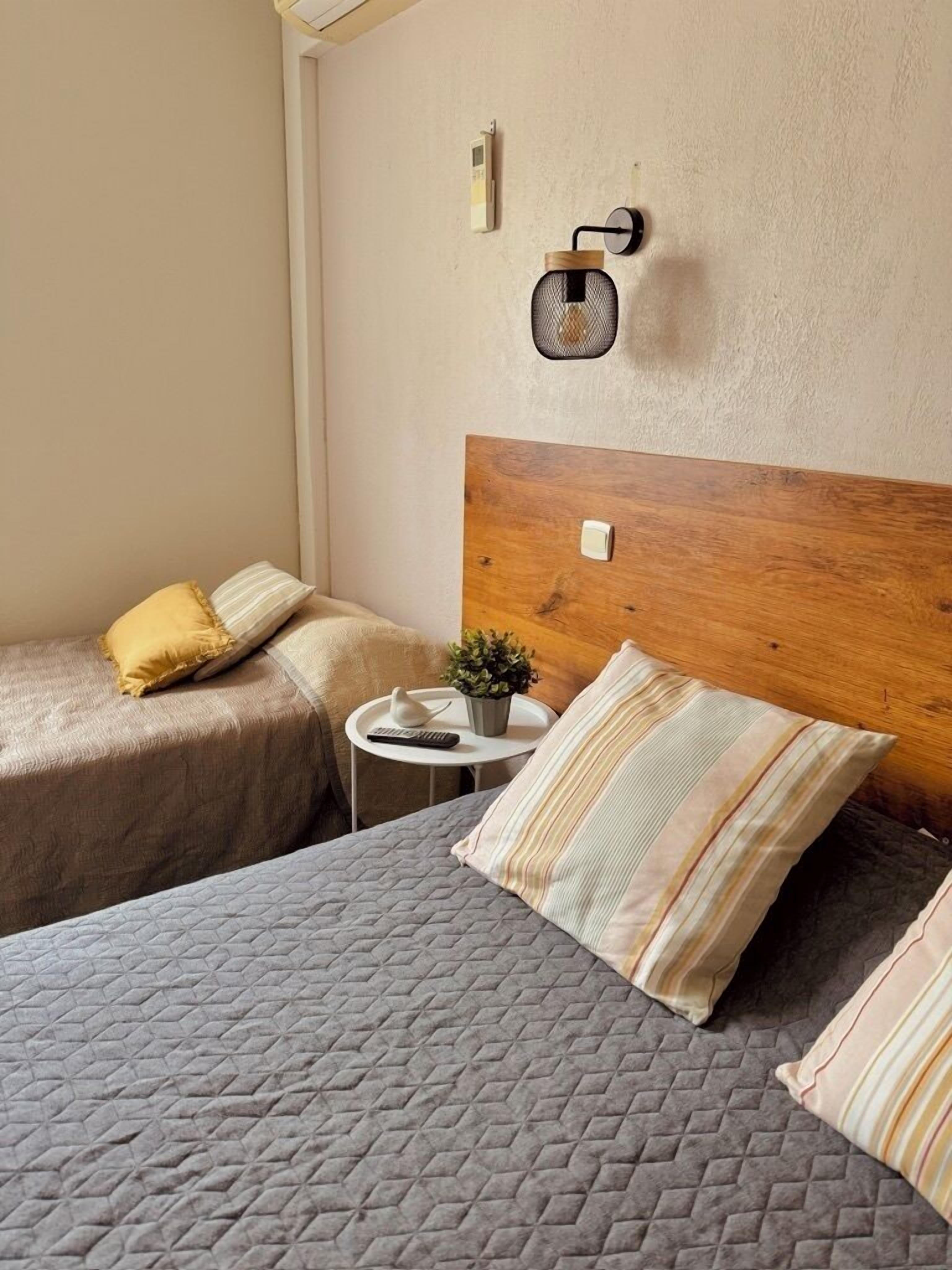 A hotel room with two beds, a small table with a plant, and a wall-mounted light fixture.