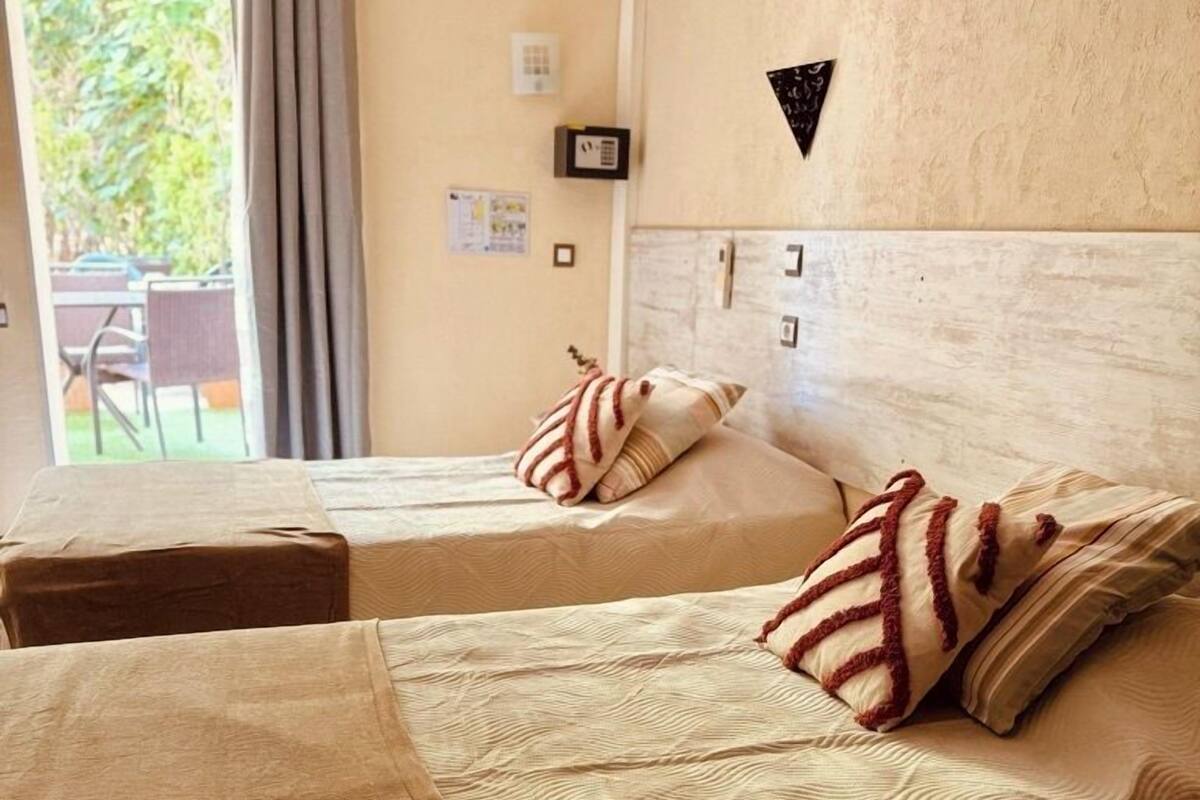 A hotel room with two beds, a small table, and a view of the outdoors.