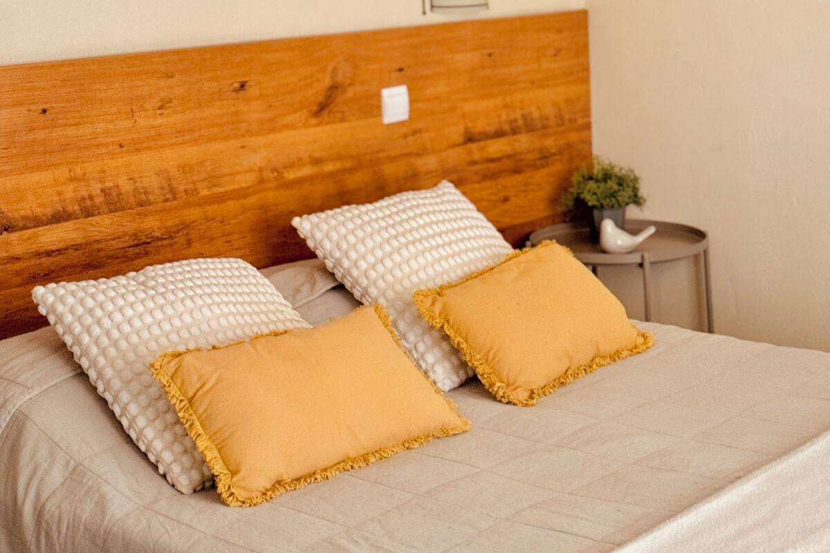 A neatly made bed with a wooden headboard, two white pillows, and two yellow pillows.
