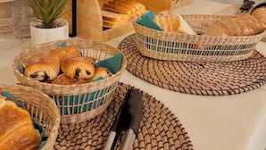 A breakfast table with wicker baskets containing pastries and bread, a framed menu, and a small potted plant. - Hôtel le Nid (Argeles-sur-Mer)
