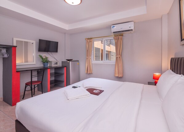 A hotel room with a bed, a desk, a chair, a TV, an air conditioner, and a window with curtains.