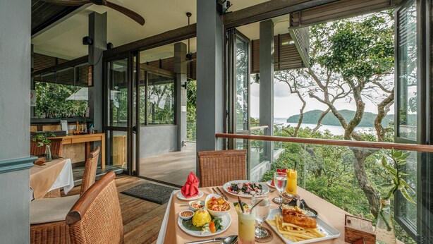 A dining area with a table set for two, featuring a meal, drinks, and a scenic view of mountains and greenery. - Ambong Rainforest Retreat (Langkawi)