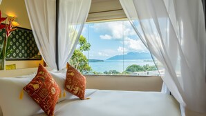 A bed with white sheets and red patterned pillows, a green patterned headboard, and a view of a lake and mountains through sheer white curtains. - Ambong Rainforest Retreat (Langkawi)