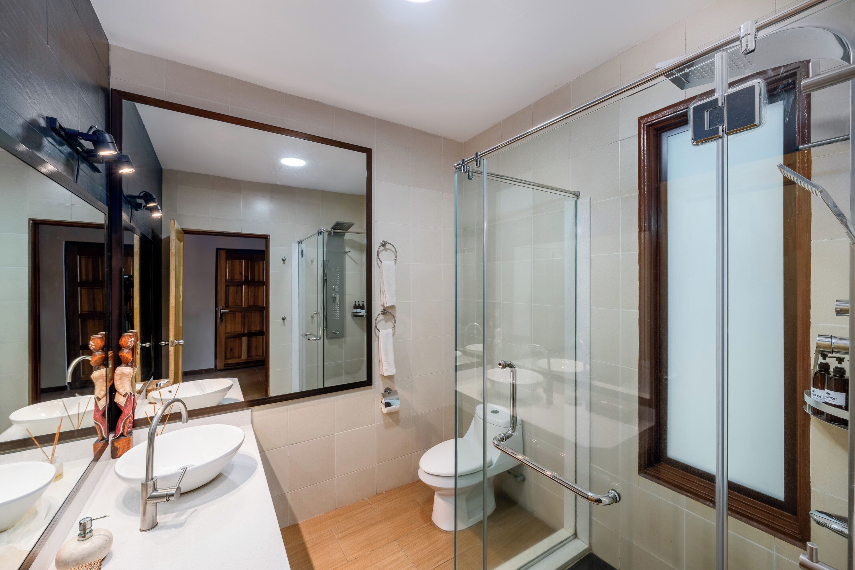 Un baño moderno con cabina de ducha de vidrio, un espejo grande y dos lavamanos.