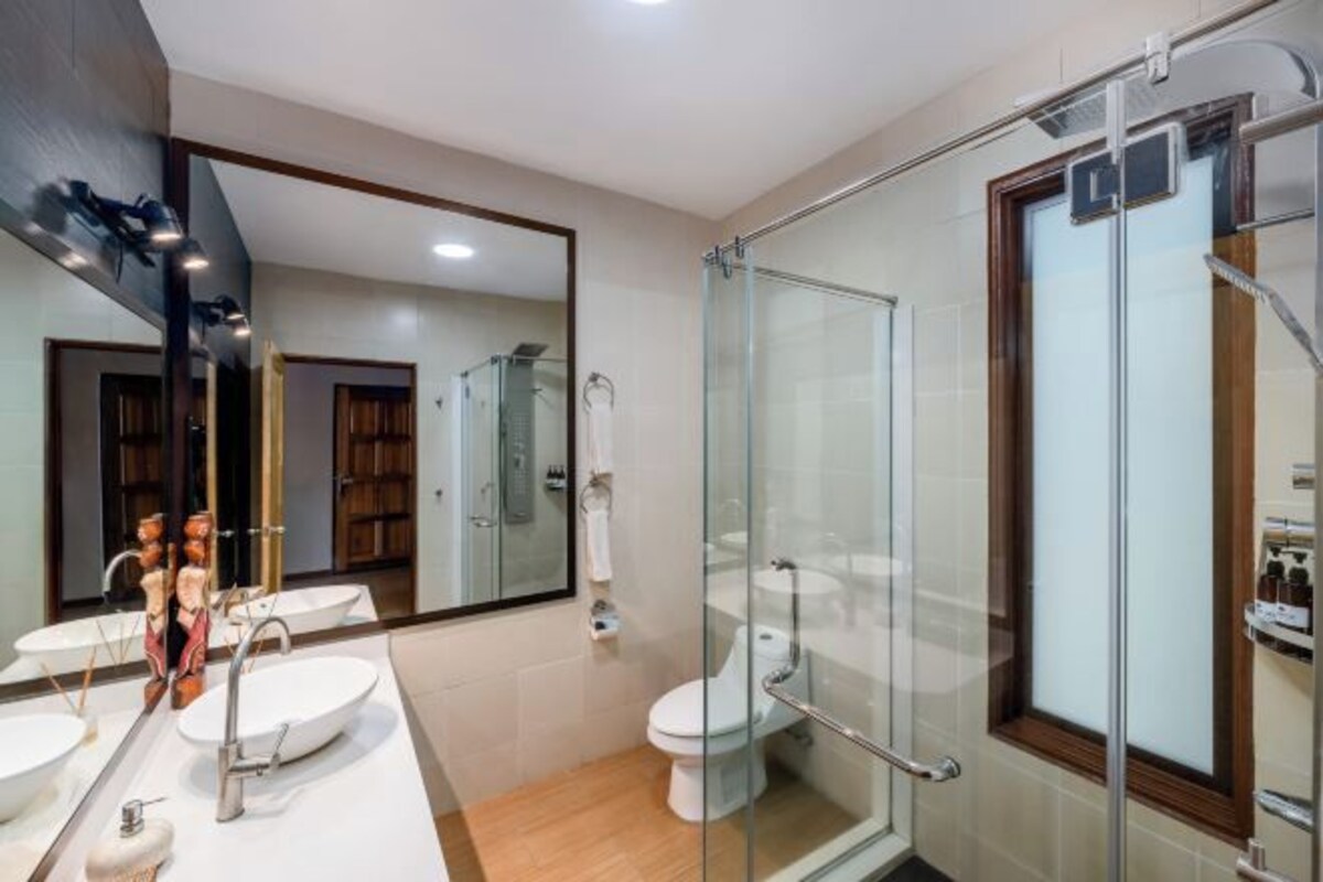 Un baño moderno con cabina de ducha de vidrio, un espejo grande y un lavamanos blanco.