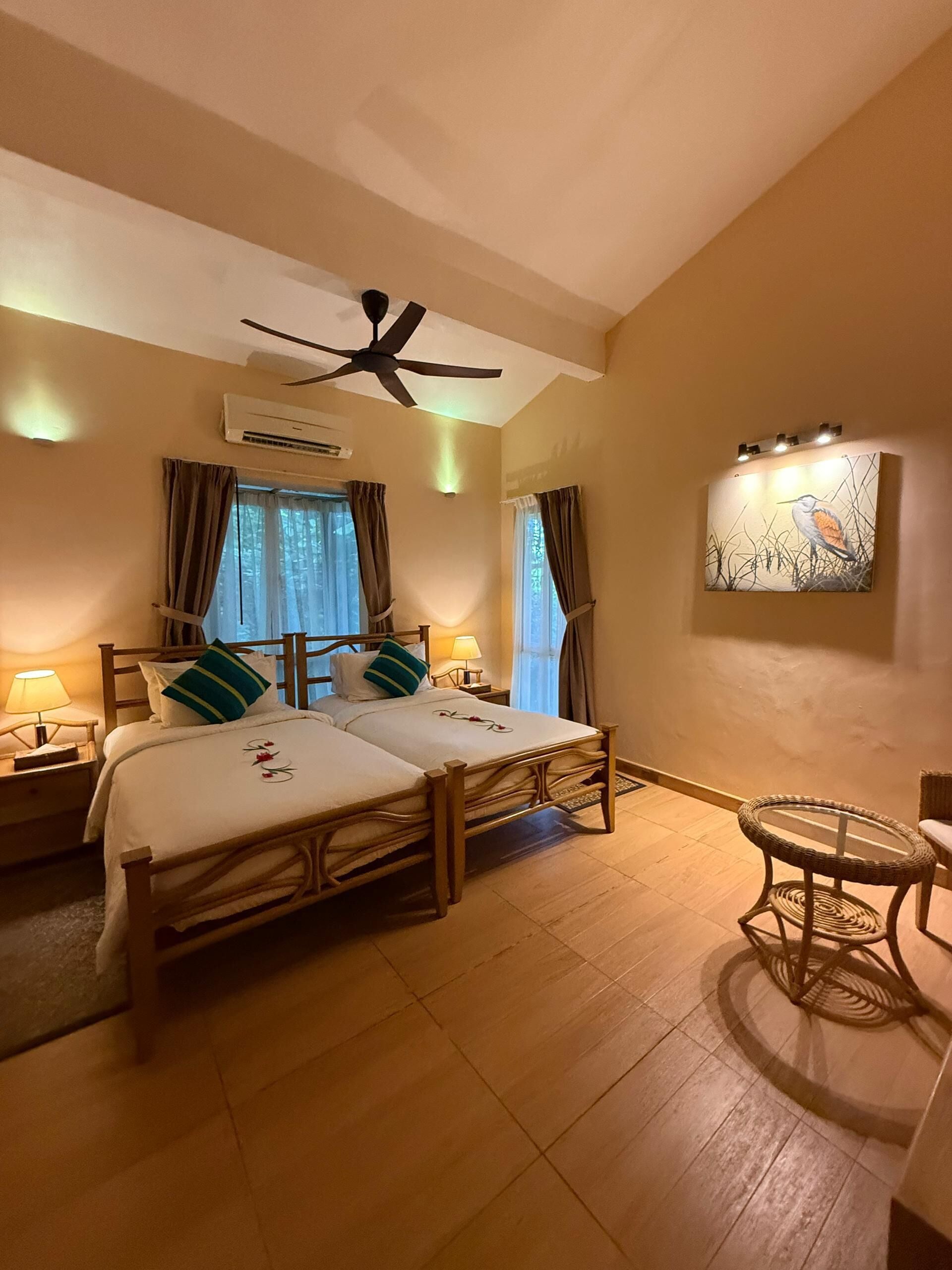 A double bed with a wooden frame, two bedside tables with lamps, a ceiling fan, and a wall-mounted air conditioner.