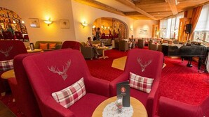 Eine Hotelhalle mit roten Sitzmöglichkeiten, einem Klavier und einer Bar.
