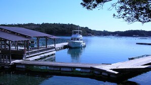 A boat docked at a pier with a covered walkway and a forested hill in the background. - Hiogiso (Shima)