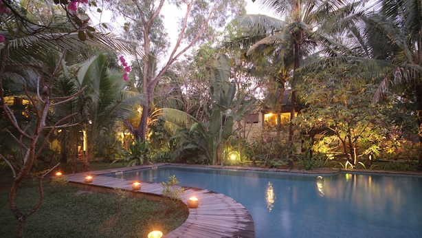 Un área de piscina tranquila con terraza de madera y velas, rodeada de exuberante vegetación tropical.