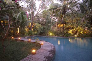 A serene pool area with a wooden deck and candles, surrounded by lush tropical vegetation.