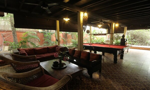 A pool area with a red pool table, wicker furniture, and a view of greenery outside.