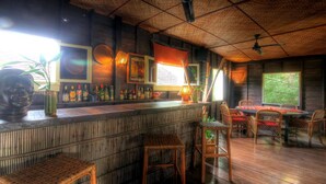Zona de bar con techo de madera, mobiliario de mimbre y vistas al exterior.
