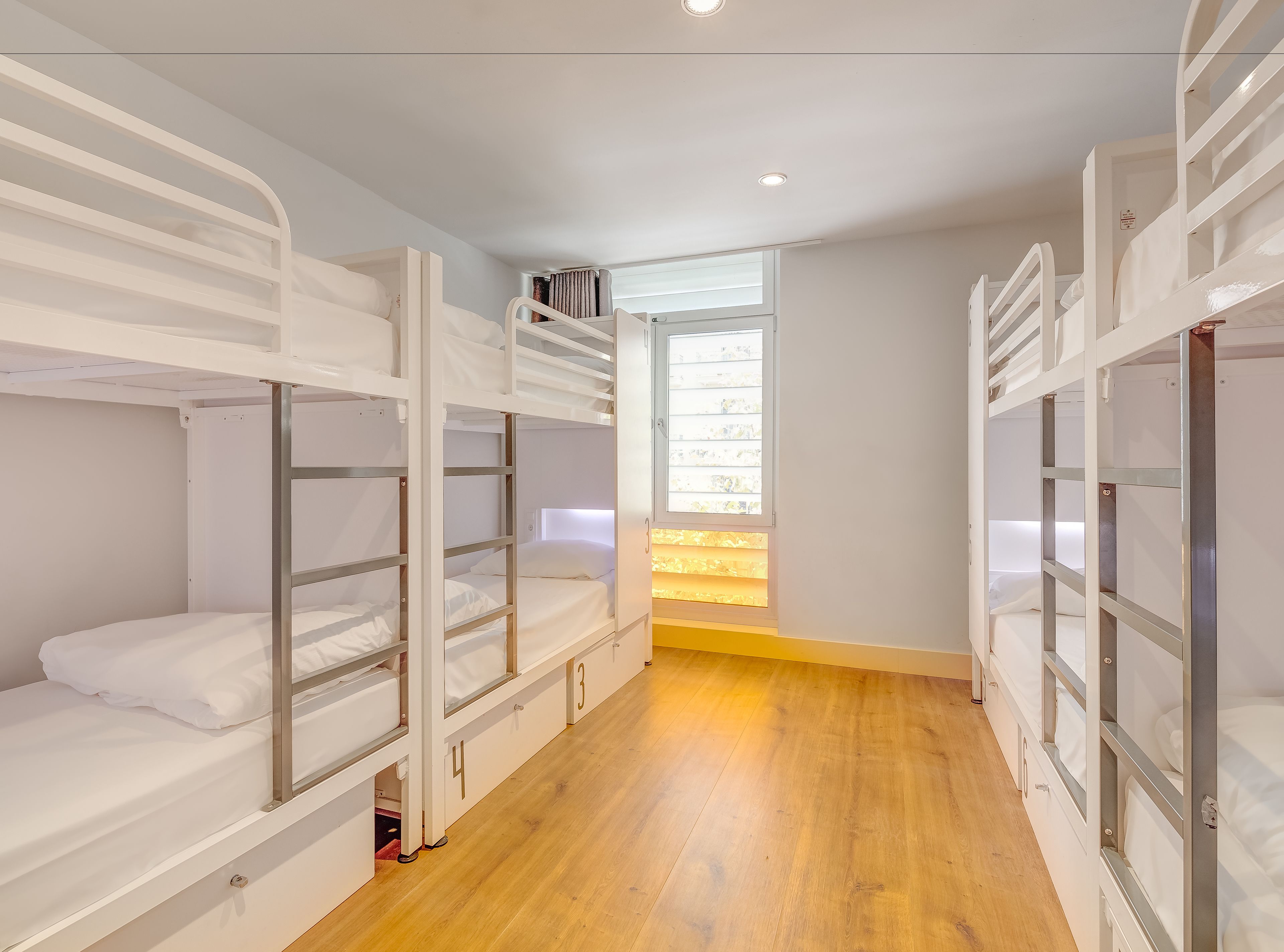 A room with bunk beds, a wooden floor, and a window with blinds.