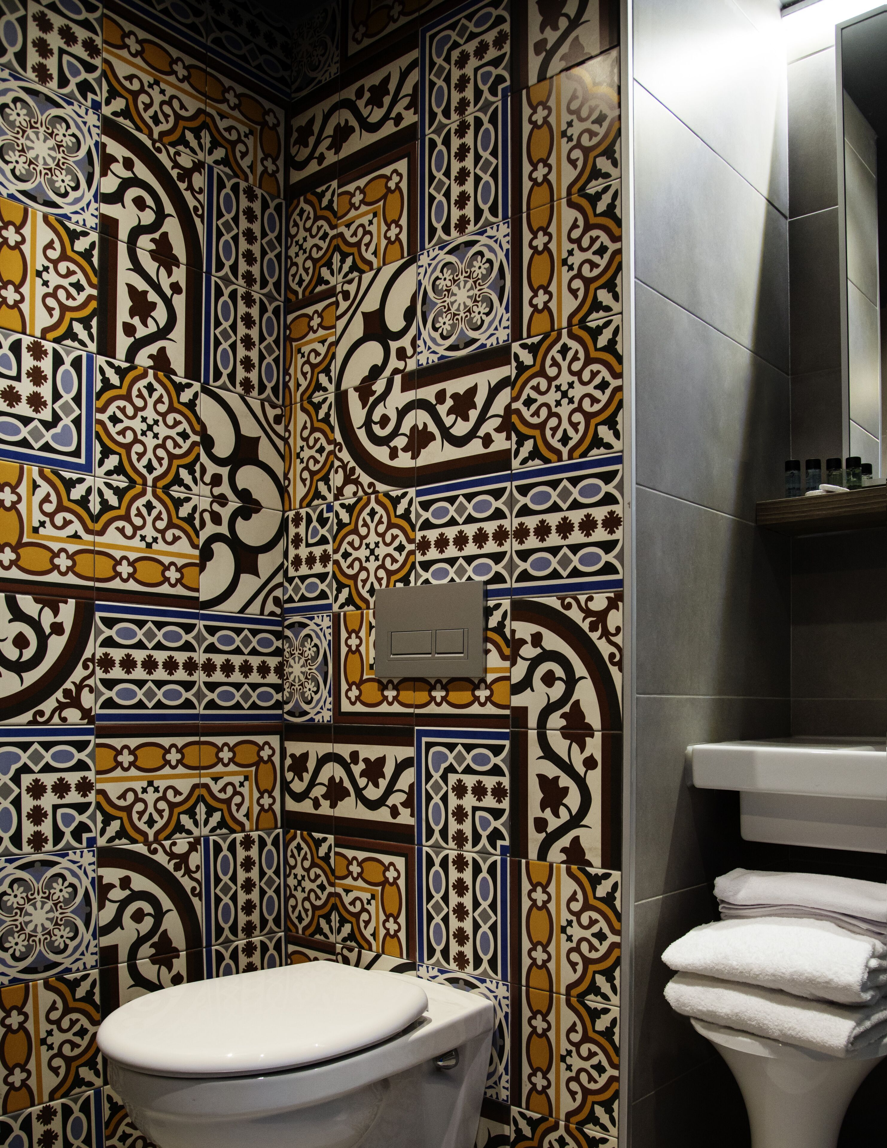 A bathroom with a toilet and a sink, both with white fixtures. The walls are tiled with a patterned design.