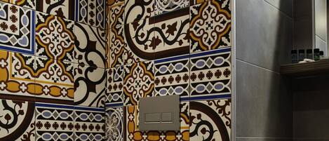 A bathroom with a toilet and a sink, both with white fixtures. The walls are tiled with a patterned design.