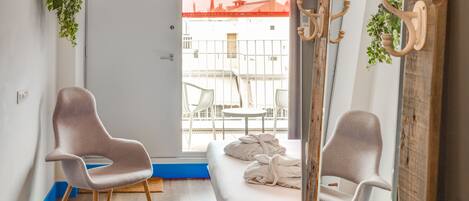 A modern hotel room with a bed, two chairs, a mirror, and a view of the outside.