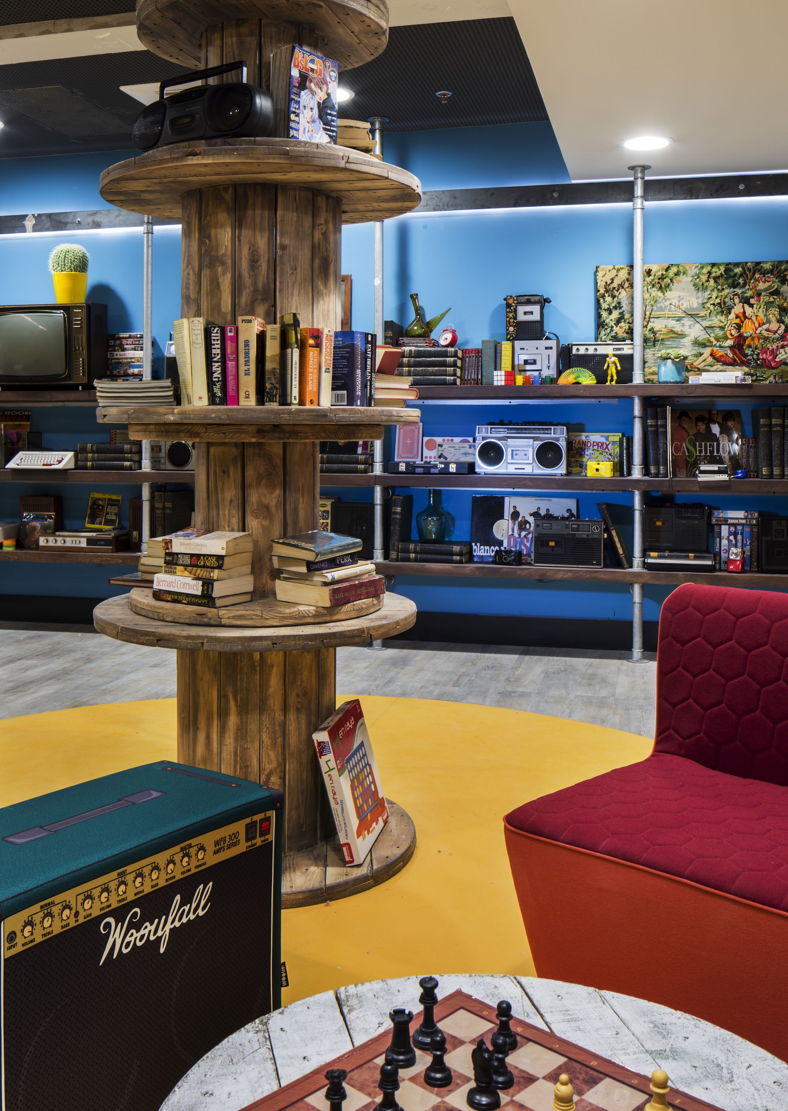 A room with a central wooden structure surrounded by bookshelves, a chessboard, and a red chair.